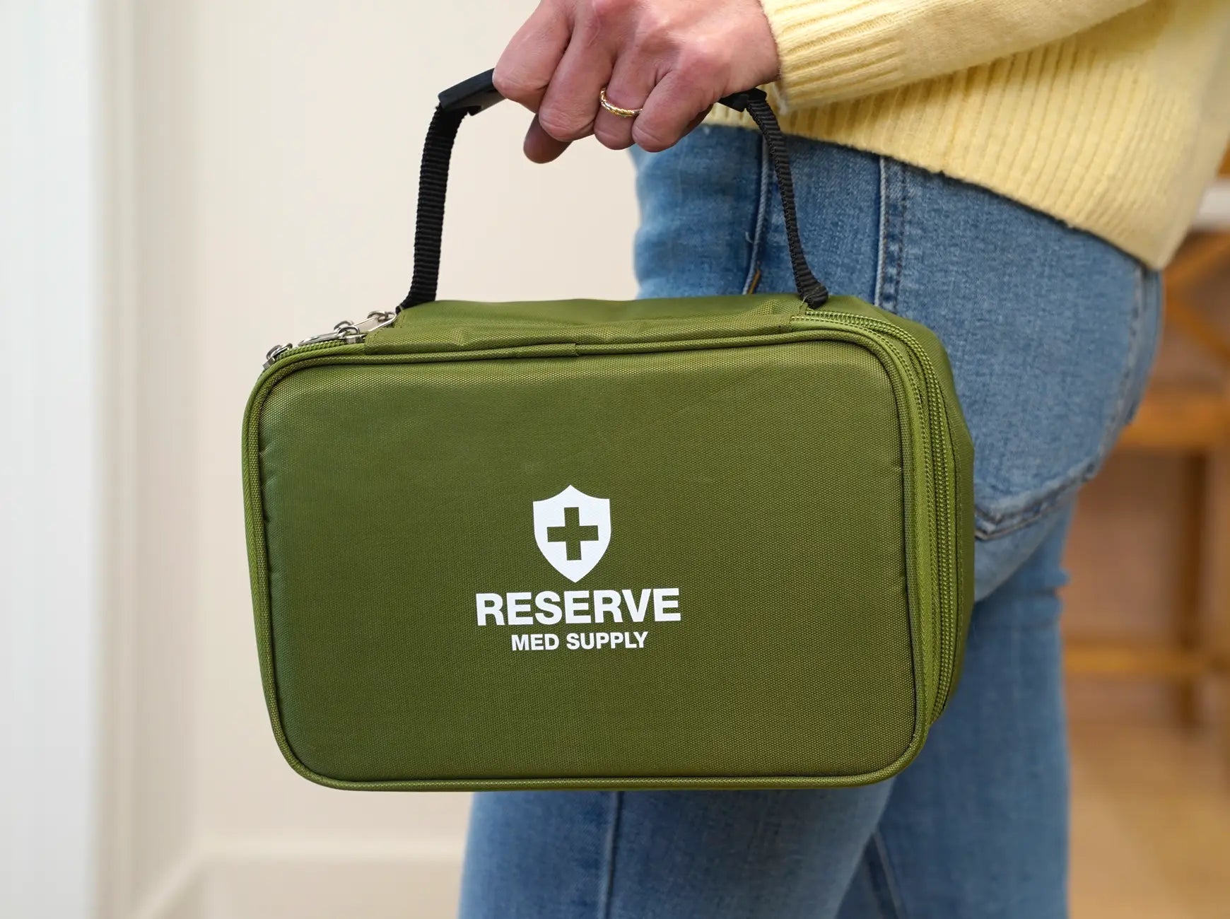 Step 3 to getting your medical kit: A close-up of a customer holding the handle of their delivered, olive green Reserve Med Supply emergency medical kit containing prescriptions filled by a licensed pharmacy and shipped to the customer's home.